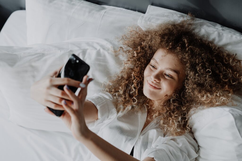 ragazza riccia mentre si scatta un selfie nel letto